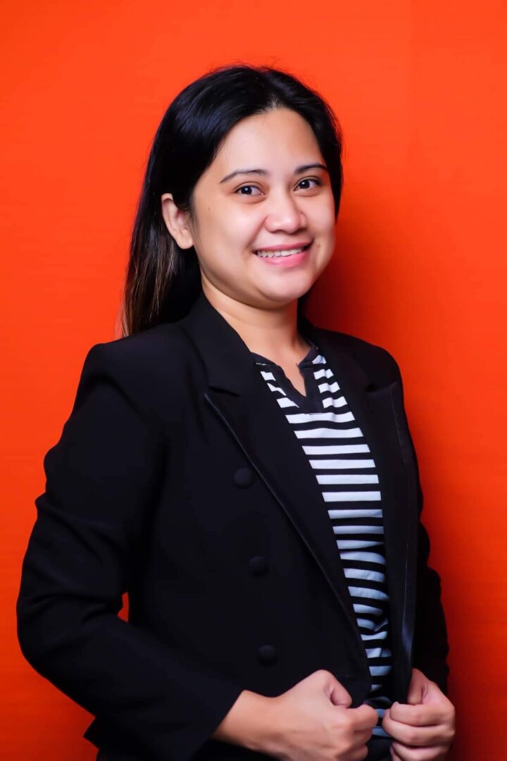 Smiling woman in black blazer, orange background.